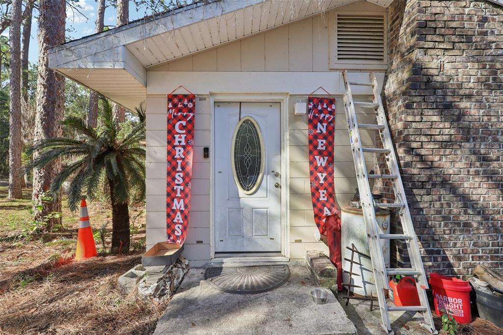 A front entrance with a white door, holiday banners, and a ladder leaning against brick — 547 SE 58TH STREET, KEYSTONE HEIGHTS, FL