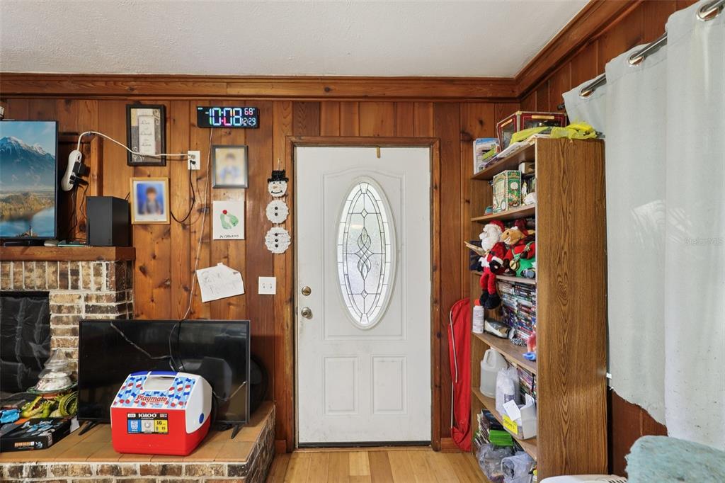 A room with wood-paneled walls, a white front door, a fireplace, and a bookshelf — 547 SE 58TH STREET, KEYSTONE HEIGHTS, FL