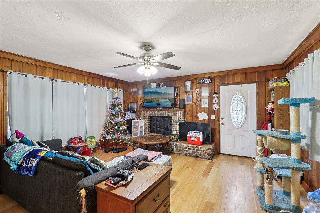 A living room features wood-paneled walls, a brick fireplace, a ceiling fan, and hardwood floors — 547 SE 58TH STREET, KEYSTONE HEIGHTS, FL