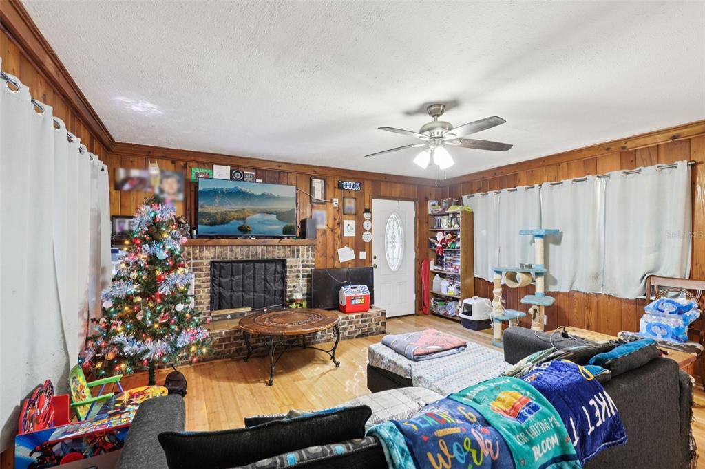 A living room features wood-paneled walls, a brick fireplace, a Christmas tree, and a ceiling fan — 547 SE 58TH STREET, KEYSTONE HEIGHTS, FL
