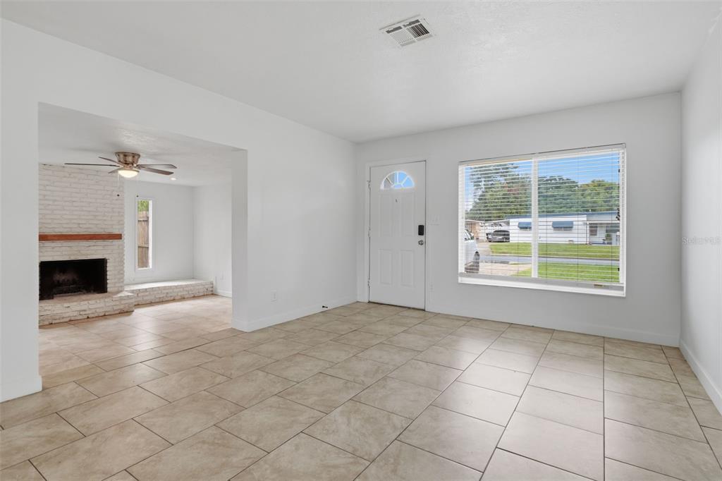 A living room with light tile flooring, a white front door, and an adjacent fireplace area — 55 RANDIA DRIVE, ORLANDO, FL