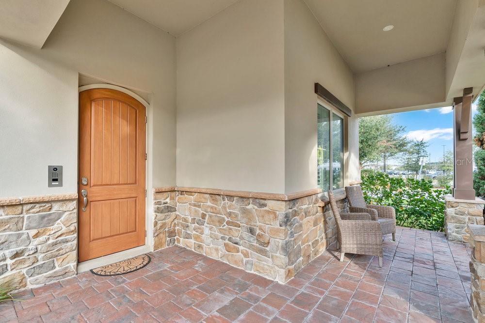A covered front porch features a wooden door, stone veneer siding, and brick paver flooring — 15607 SYLVESTER PALM DRIVE, WINTER GARDEN, FL