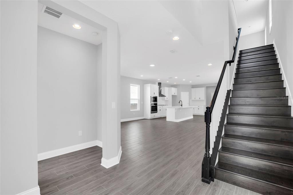 An open-concept interior features a staircase with dark wood treads and a white kitchen beyond — 12743 BRODLOVE LANE, WINTER GARDEN, FL