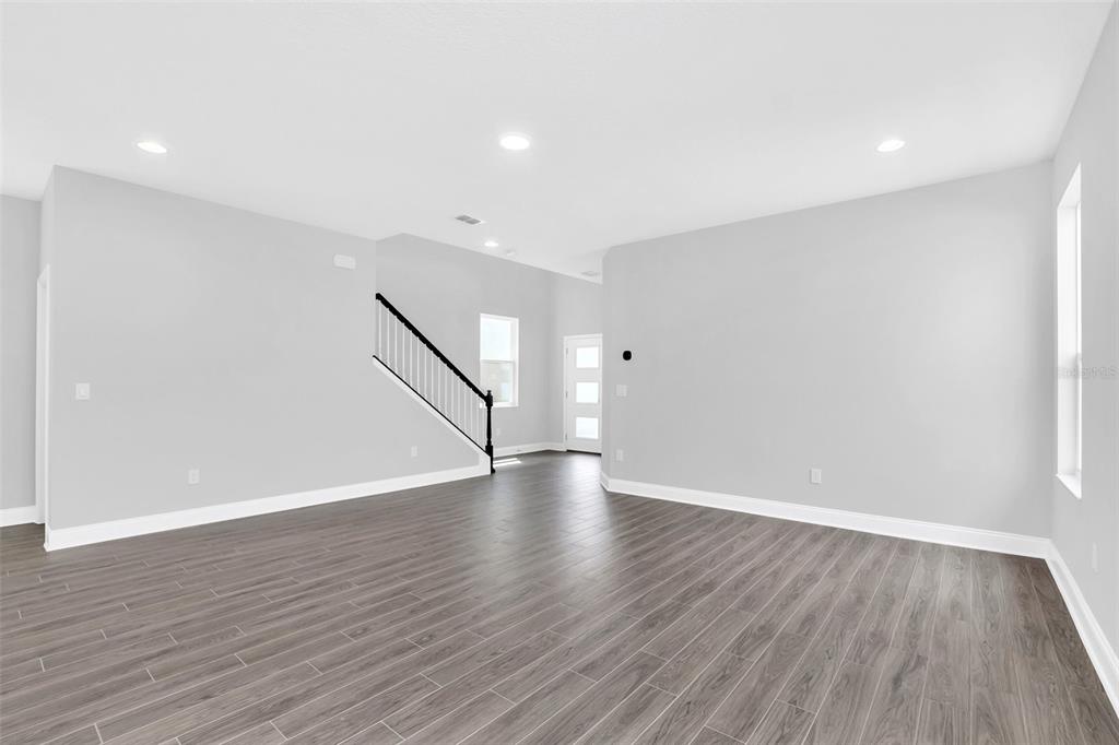 An empty living room features gray walls, dark wood-look flooring, and a staircase with railings — 12743 BRODLOVE LANE, WINTER GARDEN, FL