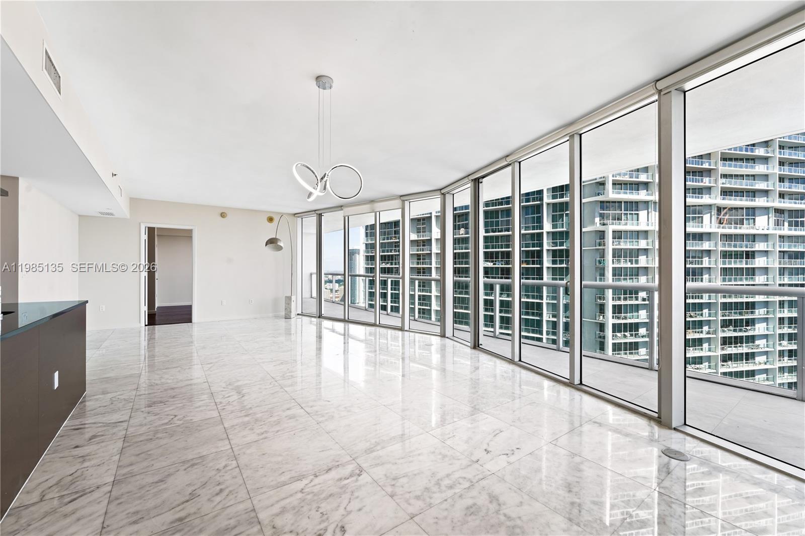 A bright, empty room features white marble floors, a modern chandelier, and floor-to-ceiling windows — 495 Brickell Ave # 3904, Miami FL 33131, MIAMI, FL