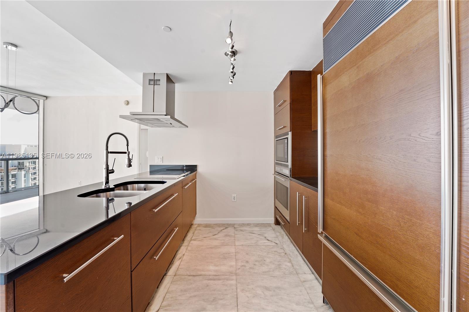 A modern kitchen features wood cabinetry, black countertops, stainless steel appliances, and marble flooring — 495 Brickell Ave # 3904, Miami FL 33131, MIAMI, FL