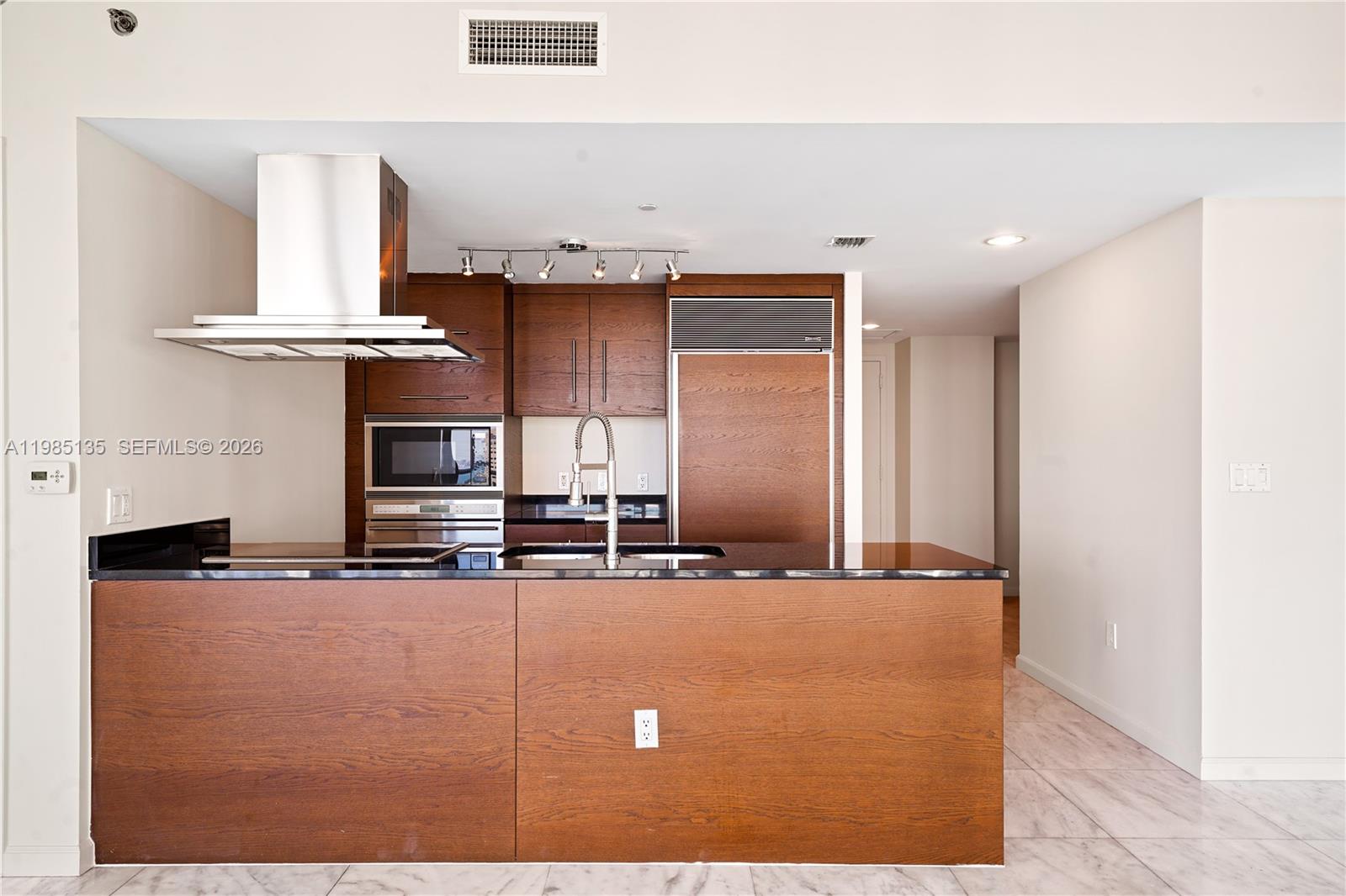 A kitchen features dark wood cabinetry, black countertops, stainless steel appliances, and light tile flooring — 495 Brickell Ave # 3904, Miami FL 33131, MIAMI, FL