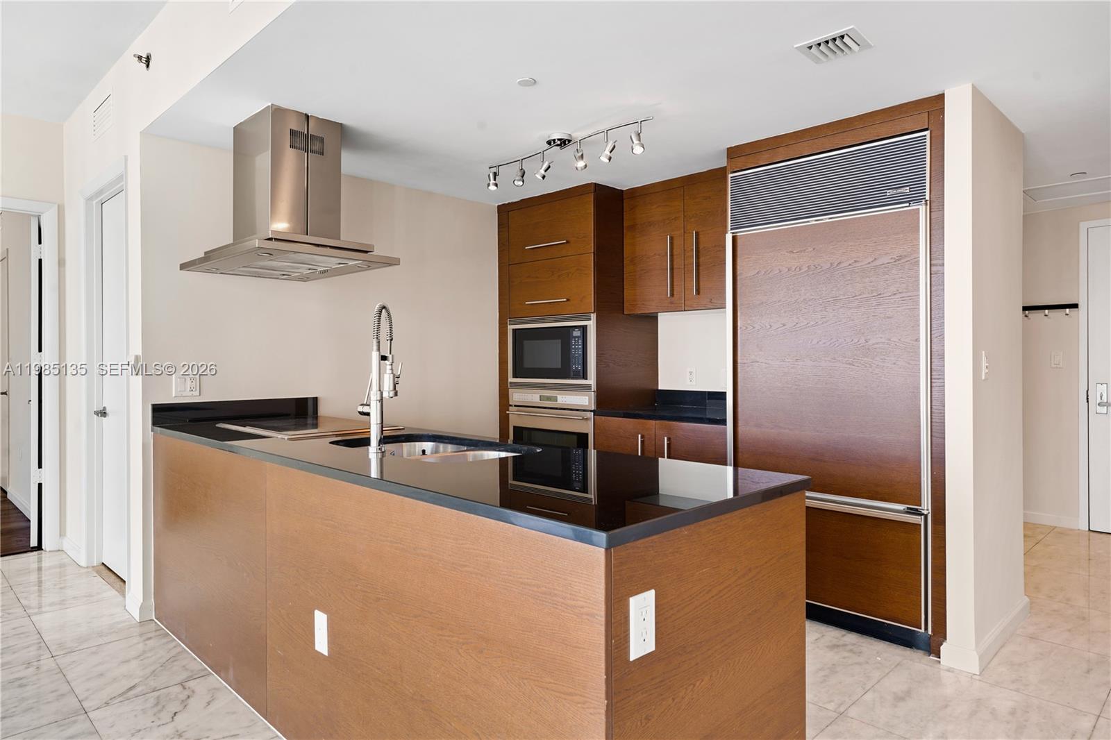 A modern kitchen features dark wood cabinetry, black countertops, and stainless steel appliances — 495 Brickell Ave # 3904, Miami FL 33131, MIAMI, FL