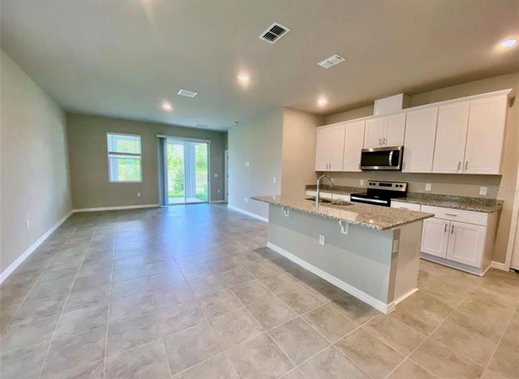 An open-concept kitchen and living area features white cabinets, granite countertops, and tile flooring — 2333 MYSTIC MAZE LANE, MINNEOLA, FL