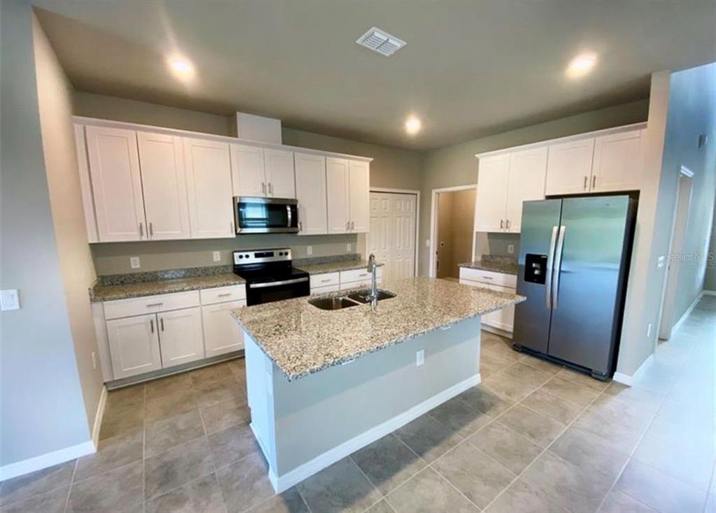 A kitchen features white cabinets, granite countertops, a central island, and stainless steel appliances — 2333 MYSTIC MAZE LANE, MINNEOLA, FL