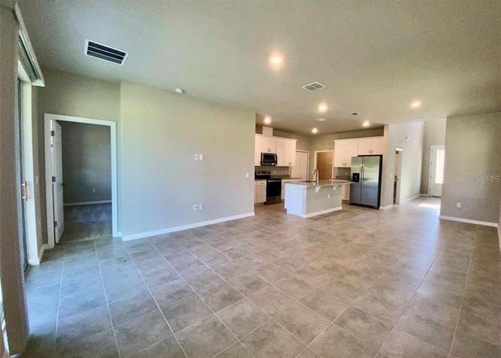 An open-concept kitchen and living area feature light tile flooring and white cabinetry — 2333 MYSTIC MAZE LANE, MINNEOLA, FL