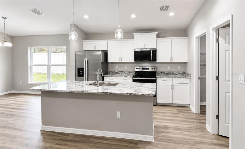 A kitchen with white cabinets, granite countertops, a center island, and stainless steel appliances — 16375 SE 80TH TERRACE, SUMMERFIELD, FL