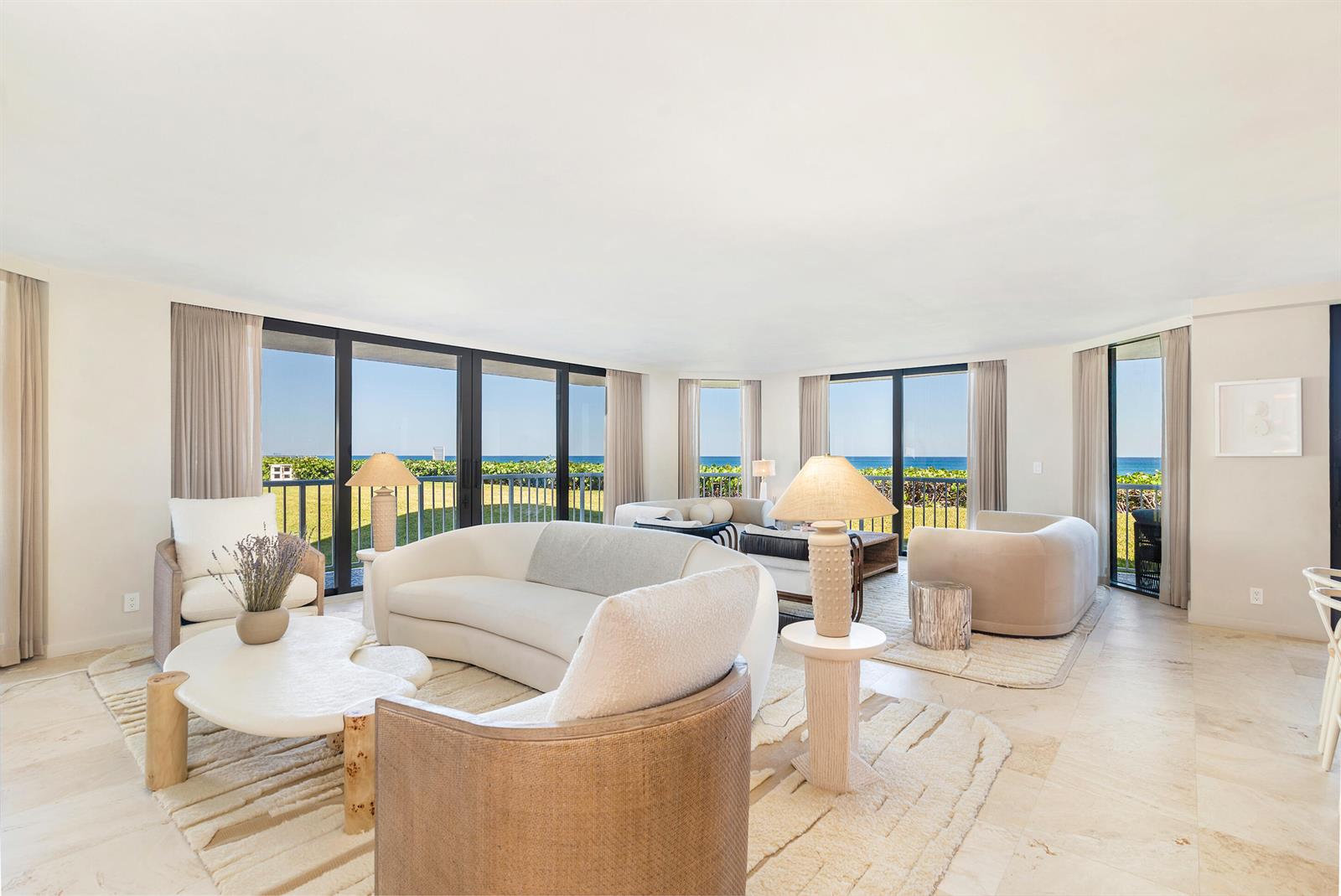 A bright living room features curved sofas, neutral furniture, and floor-to-ceiling windows overlooking the ocean — 3170 S Ocean Boulevard, Palm Beach FL 33480, PALM BEACH, FL