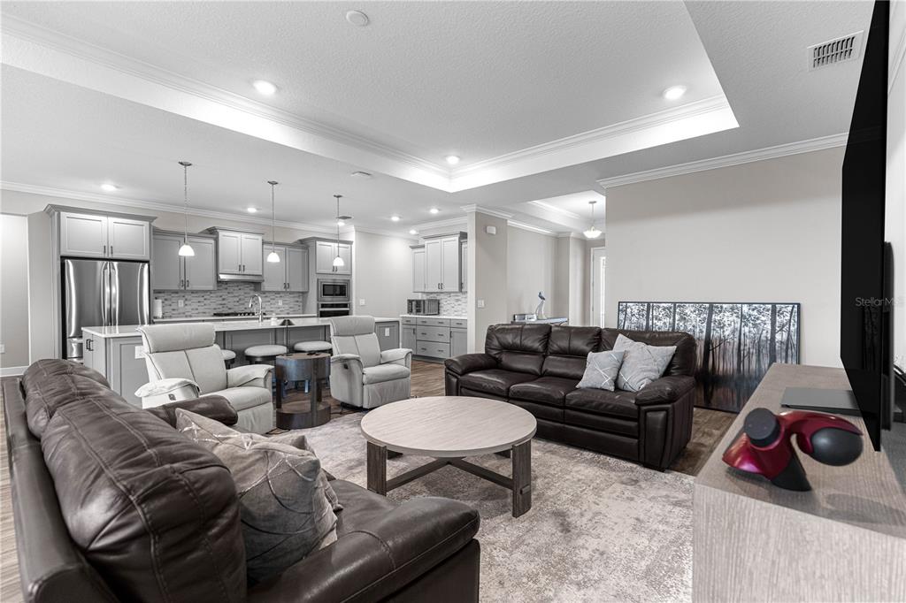 An open-concept living room features dark leather sofas, light gray recliners, and a modern kitchen — 9791 SW 82ND STREET ROAD, OCALA, FL