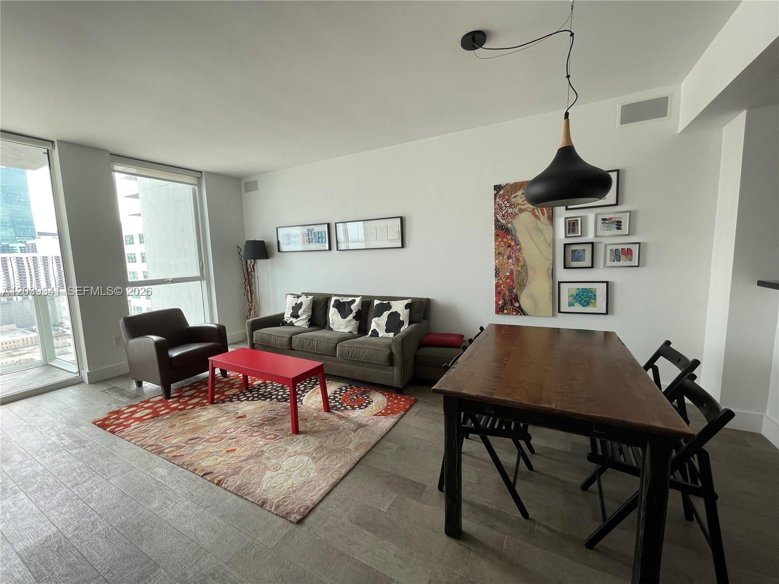 A living and dining area features a grey sofa, red coffee table, and wood table — MIAMI, FL