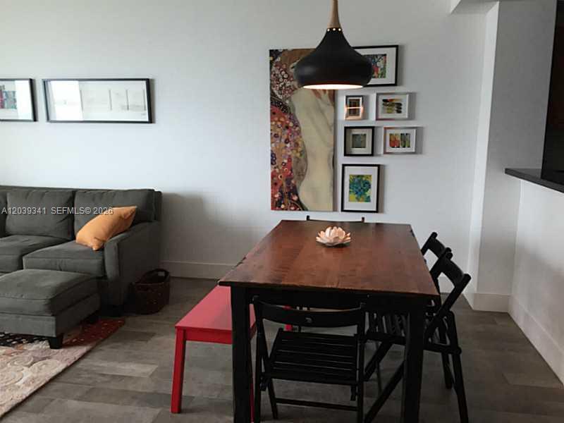 A dining area with a wooden table, black chairs, a red bench, and wall art — MIAMI, FL