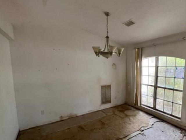 An empty room features a chandelier, a large window, and bare subflooring — 265 SE TWIG AVENUE, PORT ST LUCIE, FL