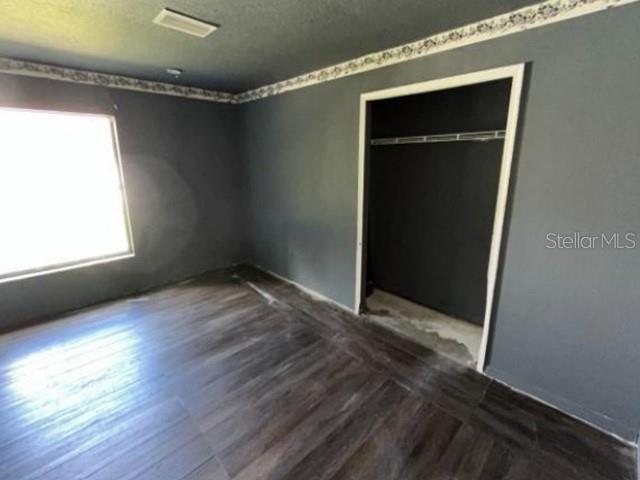 A bedroom with dark gray walls, wood-look flooring, a window, and an open closet — 265 SE TWIG AVENUE, PORT ST LUCIE, FL