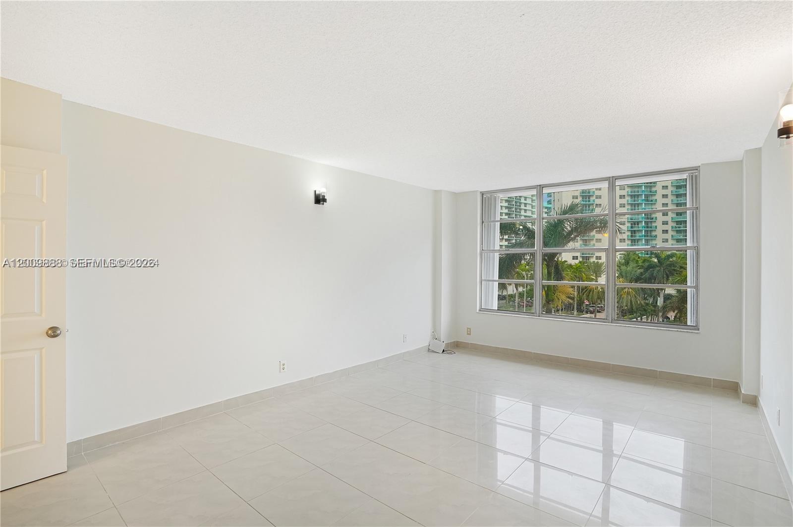 An empty room with white walls, light tile flooring, and a large window overlooking trees — 3800 S Ocean Dr # 414, Hollywood FL 33019, HOLLYWOOD, FL