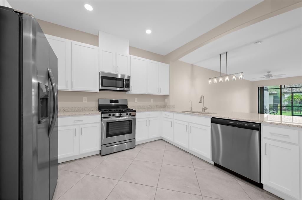 A kitchen with white cabinets, stainless steel appliances, granite countertops, and light tile flooring — 15949 CLEAR SKIES PLACE, BRADENTON, FL