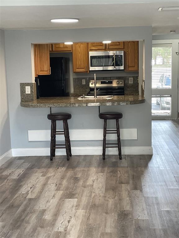 A kitchen with wood cabinets and a breakfast bar with two stools faces a living area — 5932 PEREGRINE AVENUE UNIT 22D, ORLANDO, FL