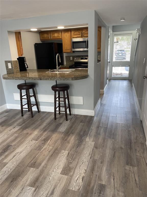 A kitchen with wood cabinets and granite countertops overlooks a living area with wood-look flooring — 5932 PEREGRINE AVENUE UNIT 22D, ORLANDO, FL