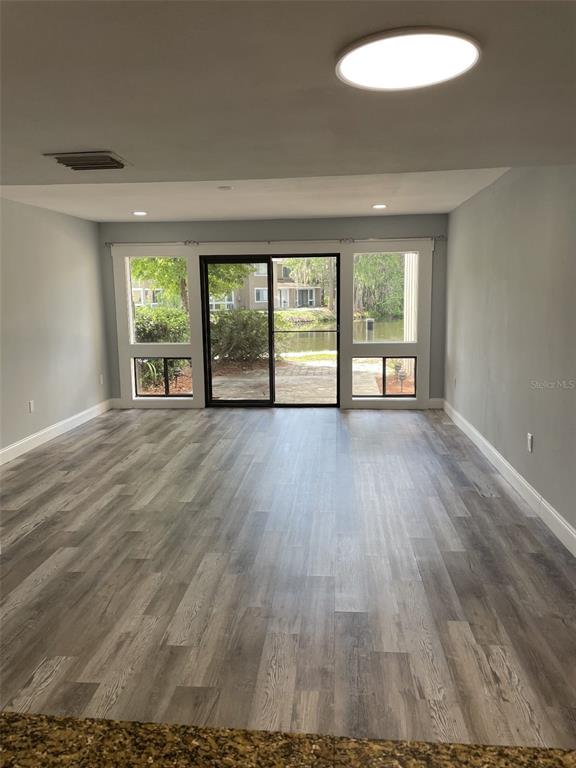An empty living room features gray wood-look flooring, a sliding glass door, and water views — 5932 PEREGRINE AVENUE UNIT 22D, ORLANDO, FL
