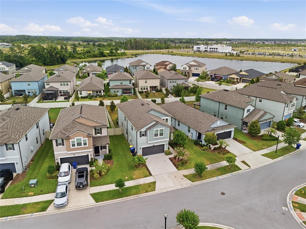 An aerial view shows a suburban neighborhood with houses, driveways, and a nearby lake — 8882 FLOURISH DRIVE, LAND O LAKES, FL