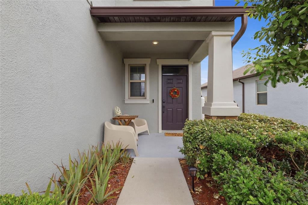 A covered front porch features a dark door, two chairs, and a small table — 8882 FLOURISH DRIVE, LAND O LAKES, FL