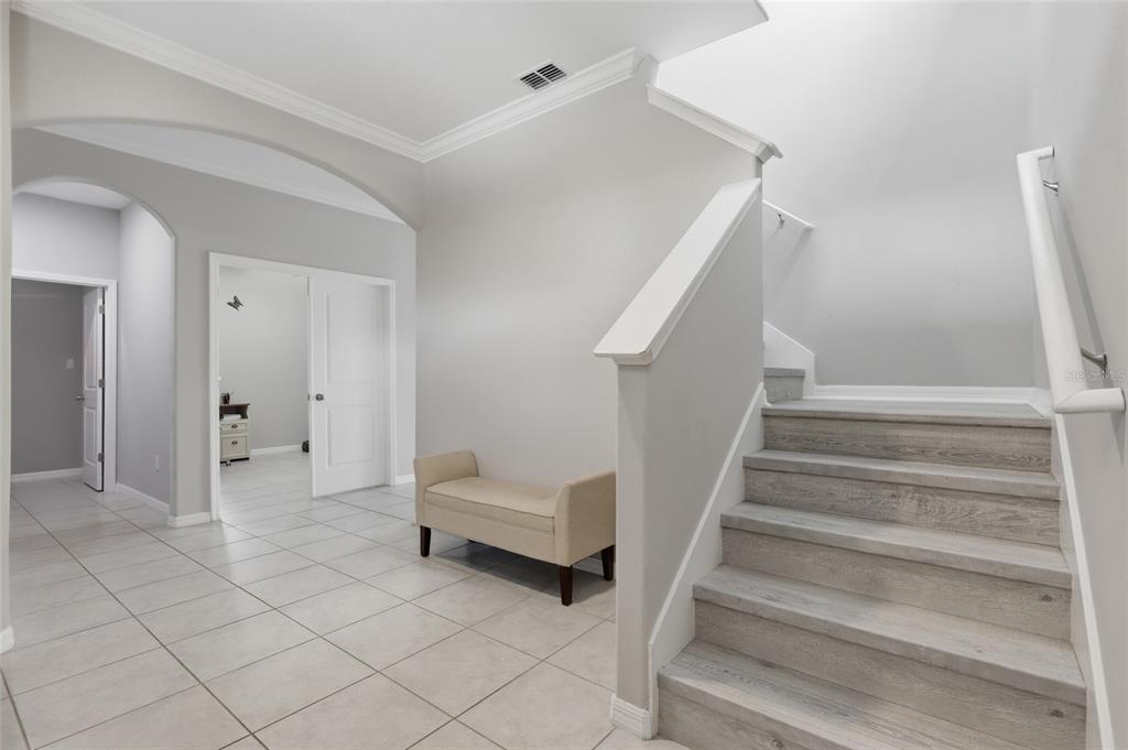 An entryway features light tile flooring, a beige bench, and stairs with wood-look treads — 8882 FLOURISH DRIVE, LAND O LAKES, FL