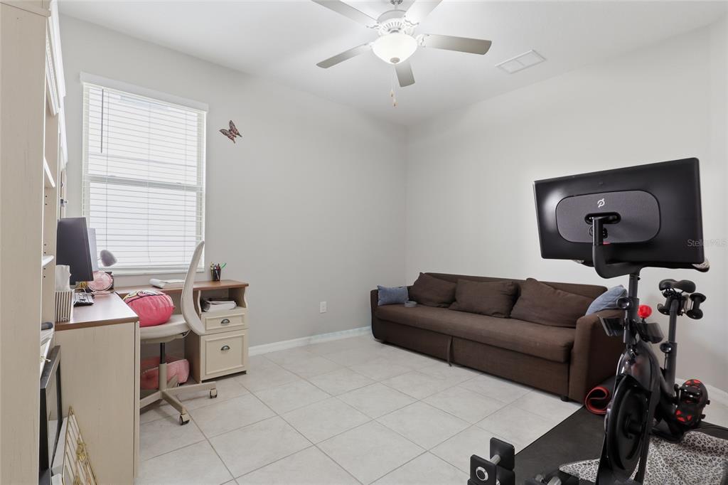 A room with tile flooring, a desk, a brown sofa, and a stationary exercise bike — 8882 FLOURISH DRIVE, LAND O LAKES, FL