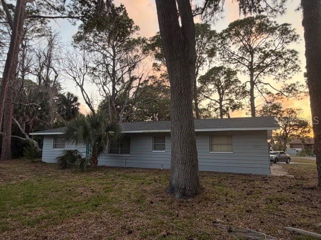 A single-story house with gray siding sits among tall trees at sunset — 7109 OELSNER STREET, NEW PORT RICHEY, FL