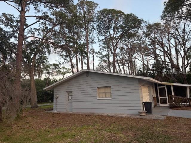 A side view of a gray, single-story house with a garage and surrounding pine trees — 7109 OELSNER STREET, NEW PORT RICHEY, FL