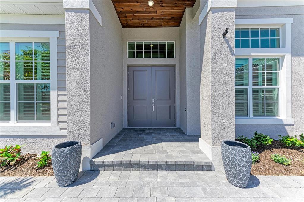 A gray double front door is centered under a covered entryway with stone pavers — 17215 ALBATROSS ROAD, VENICE, FL
