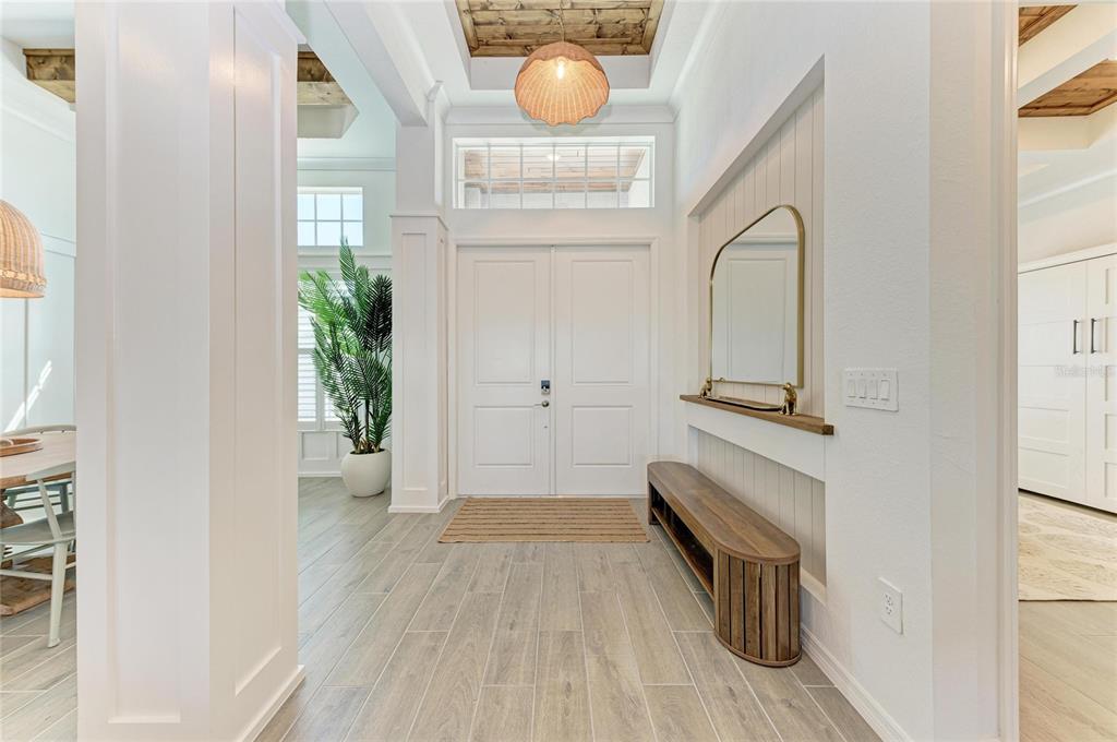 A bright entryway features white double doors, wood-look tile flooring, and a built-in wooden bench — 17215 ALBATROSS ROAD, VENICE, FL
