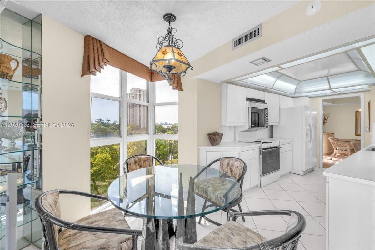 A dining area with a glass table and chairs sits adjacent to a white kitchen — 1000 Quayside Ter # 701, Miami FL 33138, MIAMI, FL