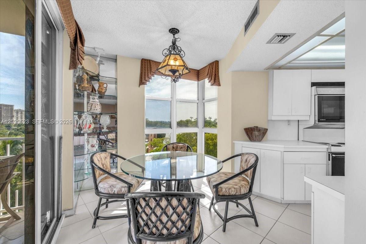 A dining area features a glass table, wicker chairs, a chandelier, and floor-to-ceiling windows — 1000 Quayside Ter # 701, Miami FL 33138, MIAMI, FL
