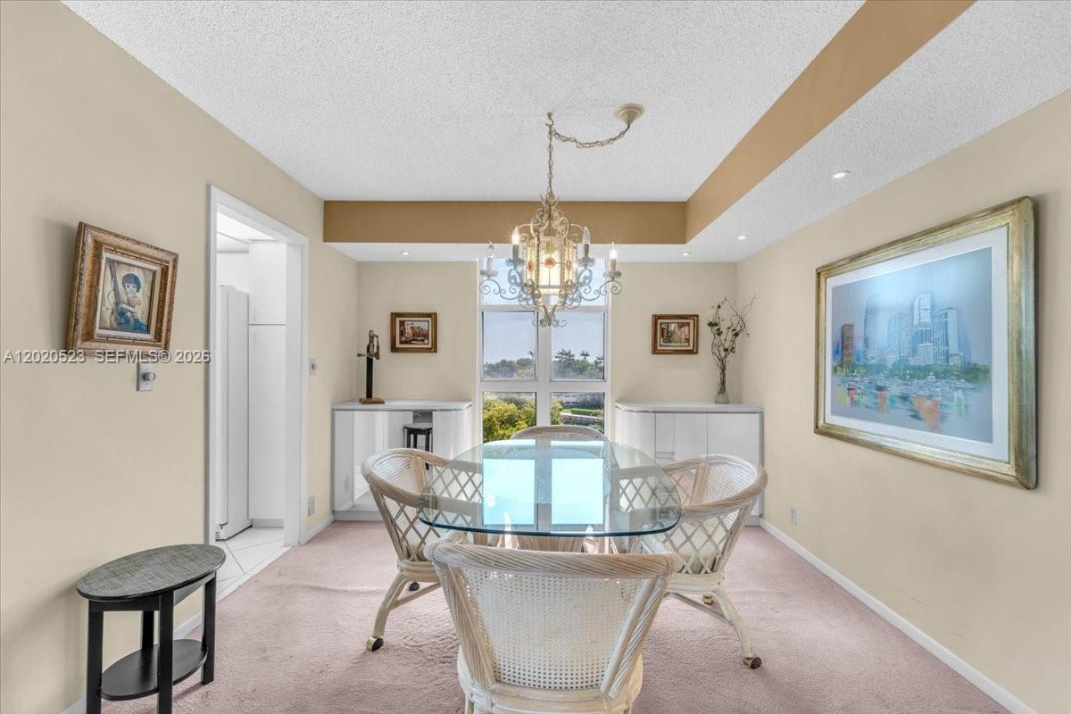 A dining room features a glass-topped table, wicker chairs, a chandelier, and framed artwork — 1000 Quayside Ter # 701, Miami FL 33138, MIAMI, FL