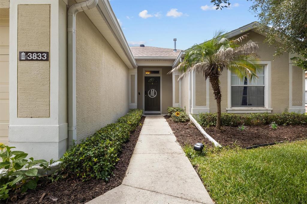 A concrete walkway leads to the front entrance of a single-story house with stucco siding — 3833 WHISTLEWOOD CIRCLE, LAKELAND, FL