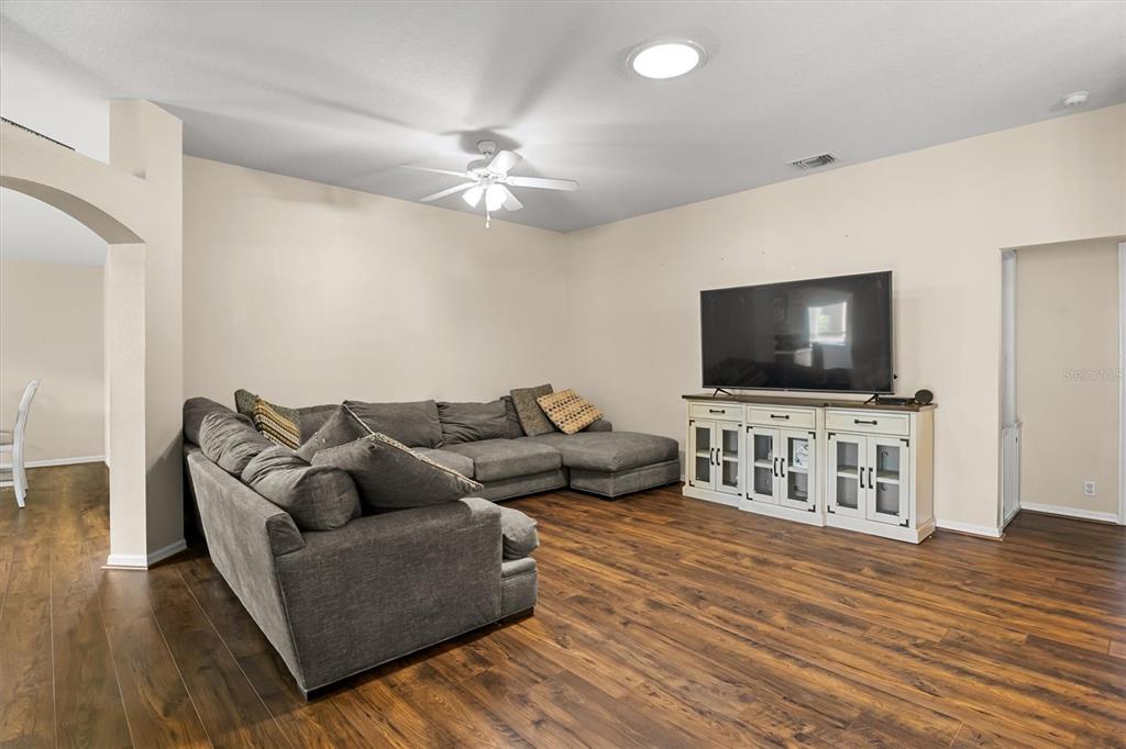 A living room features a large gray sectional sofa, a television console, and wood flooring — 3833 WHISTLEWOOD CIRCLE, LAKELAND, FL