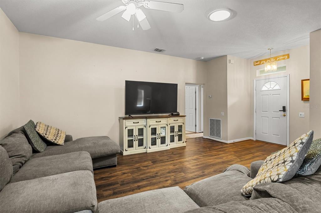 A living room features a grey sectional sofa, a television on a console, and wood flooring — 3833 WHISTLEWOOD CIRCLE, LAKELAND, FL