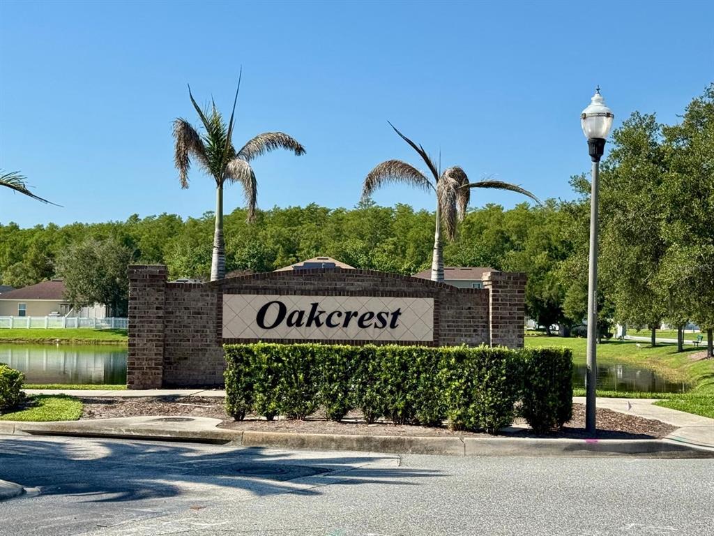 A brick monument sign reading Oakcrest stands in front of palm trees and a pond — 561 CRESTING OAK CIRCLE UNIT 86, ORLANDO, FL