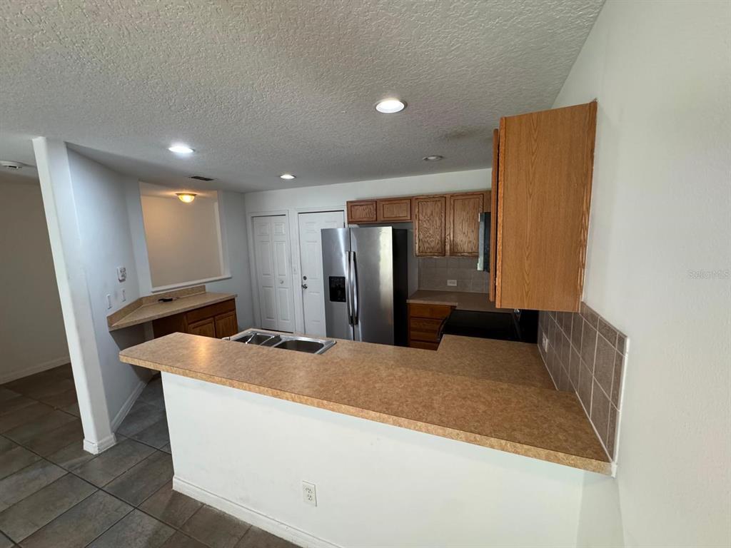 A kitchen features a breakfast bar, stainless steel refrigerator, and light-colored laminate countertops — 561 CRESTING OAK CIRCLE UNIT 86, ORLANDO, FL