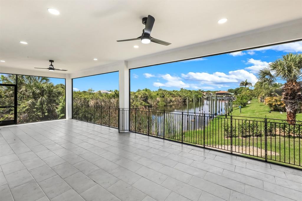 A covered patio with light gray tile flooring overlooks a canal and grassy yard — 14395 AURELLA CIRCLE, PORT CHARLOTTE, FL