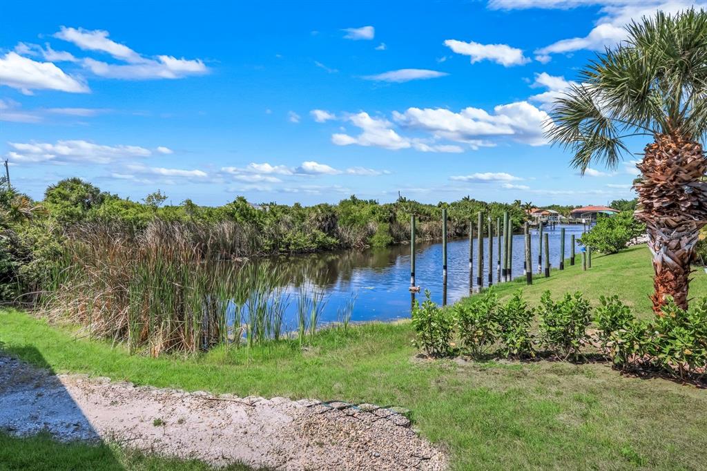 A grassy backyard overlooks a narrow canal lined with tall reeds and wooden pilings — 14395 AURELLA CIRCLE, PORT CHARLOTTE, FL
