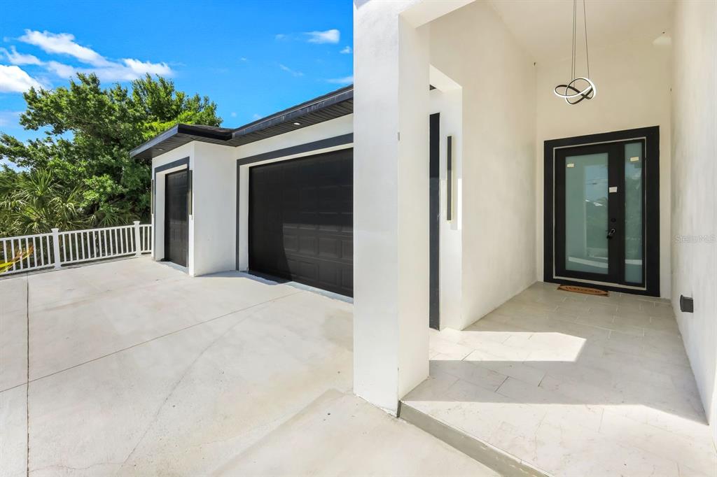 A modern home exterior features a white facade, black garage doors, and a covered entryway — 14395 AURELLA CIRCLE, PORT CHARLOTTE, FL