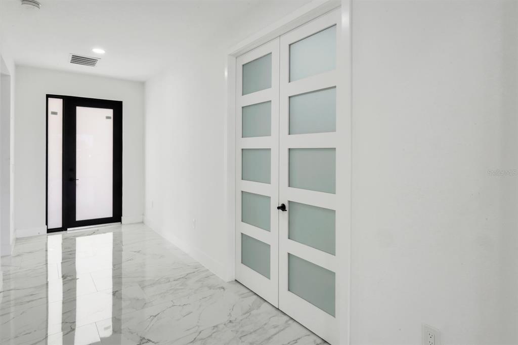 A white hallway features marble-look tile flooring, a black-framed front door, and white French doors — 14395 AURELLA CIRCLE, PORT CHARLOTTE, FL