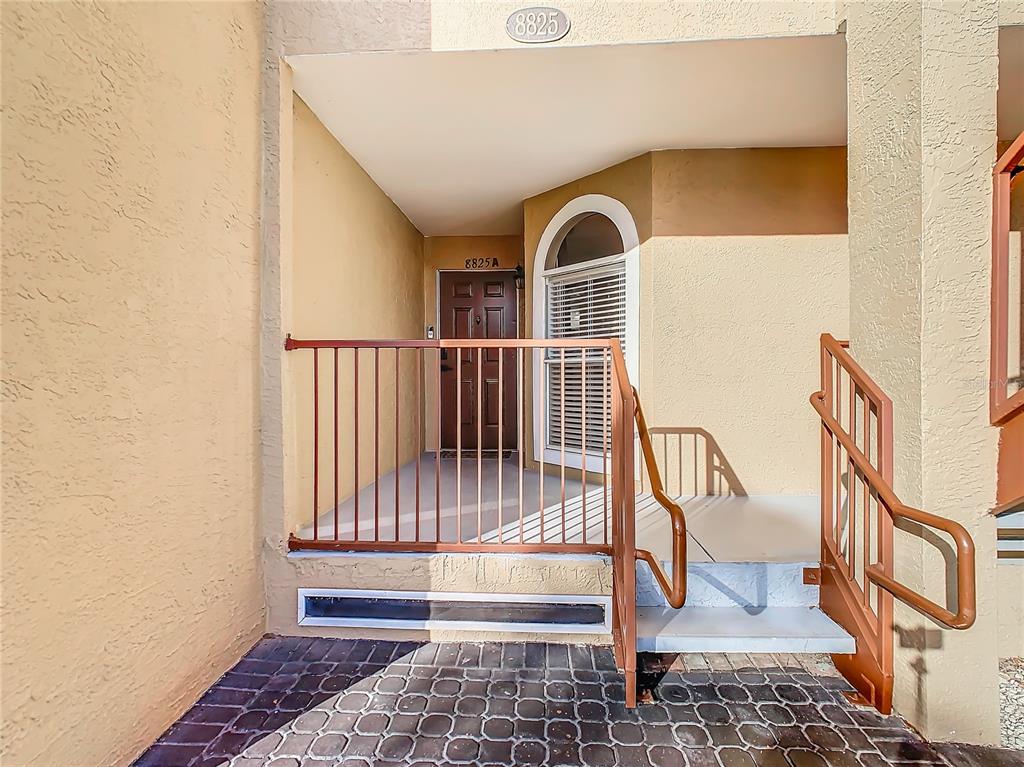 The exterior entrance features a brown door, a metal railing, and a paved walkway — 8825 CORAL PALMS COURT UNIT A, KISSIMMEE, FL