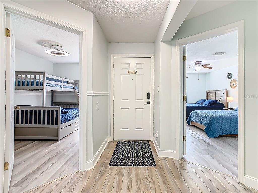 A hallway with light wood flooring leads to a front door between two bedrooms — 8825 CORAL PALMS COURT UNIT A, KISSIMMEE, FL