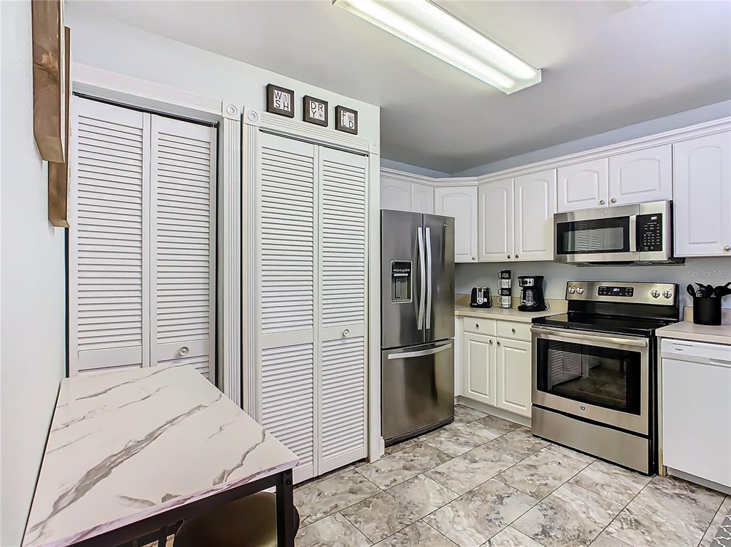 A kitchen features white cabinets, stainless steel appliances, louvered closet doors, and marble-patterned tile flooring — 8825 CORAL PALMS COURT UNIT A, KISSIMMEE, FL